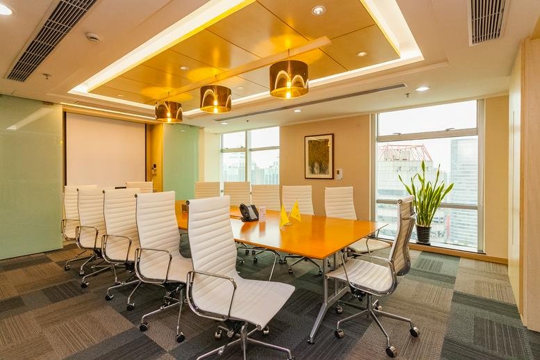Professional boardroom with a large light-wood table, white leather chairs, and pendant lighting.