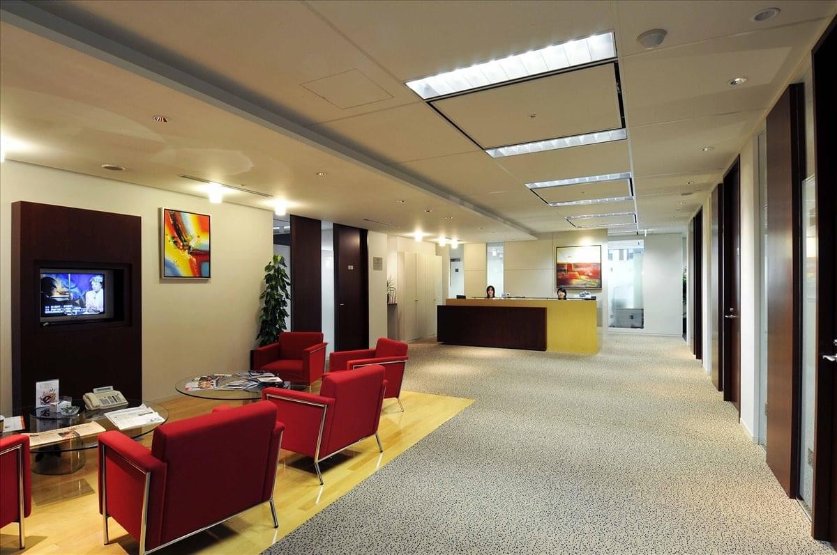 Spacious reception lounge with vibrant red armchairs and a warm wood floor.