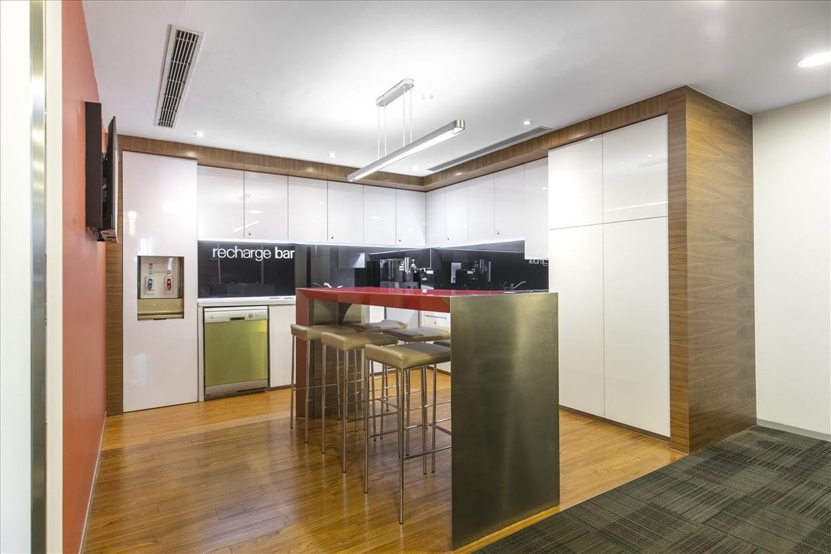 Modern communal kitchen and breakout area with wooden floors and a red bar counter.