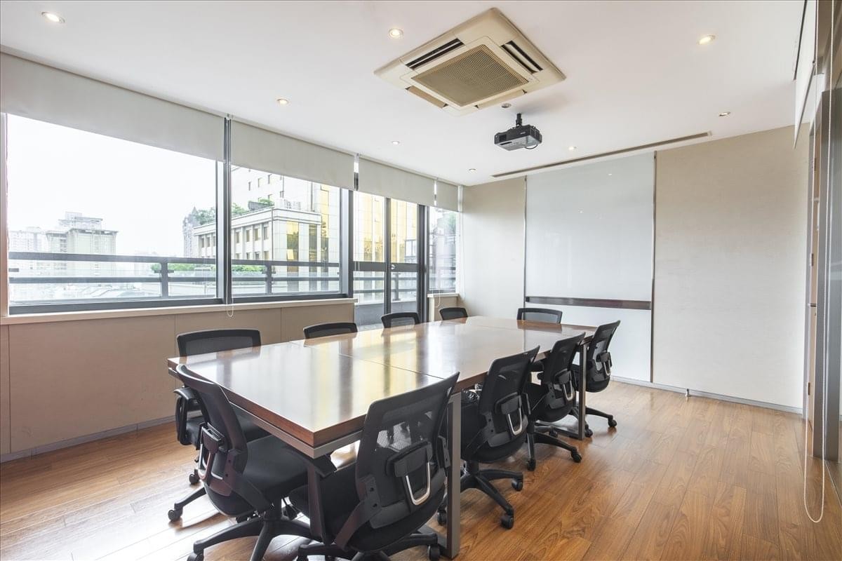 Bright conference room featuring a large wood-finish table, black rolling chairs, and city views.