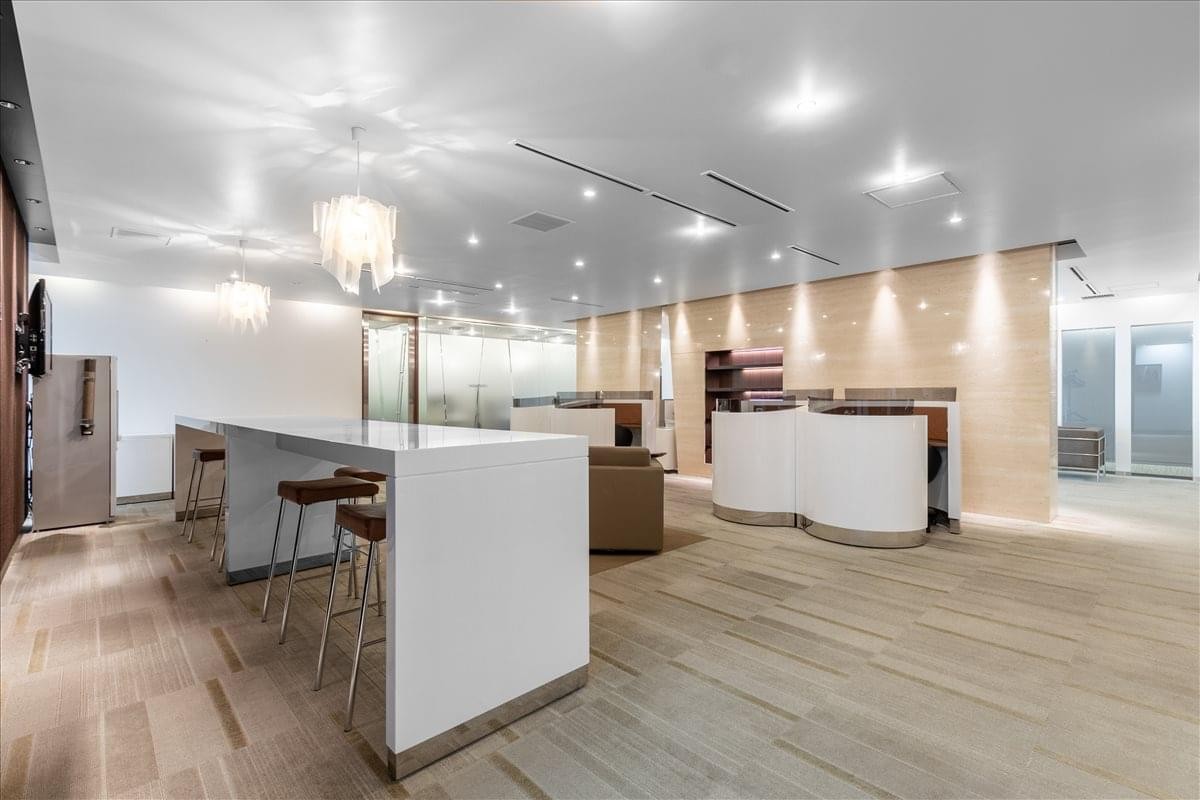 Communal break area with a high white breakfast bar, stools, and warm wood flooring.