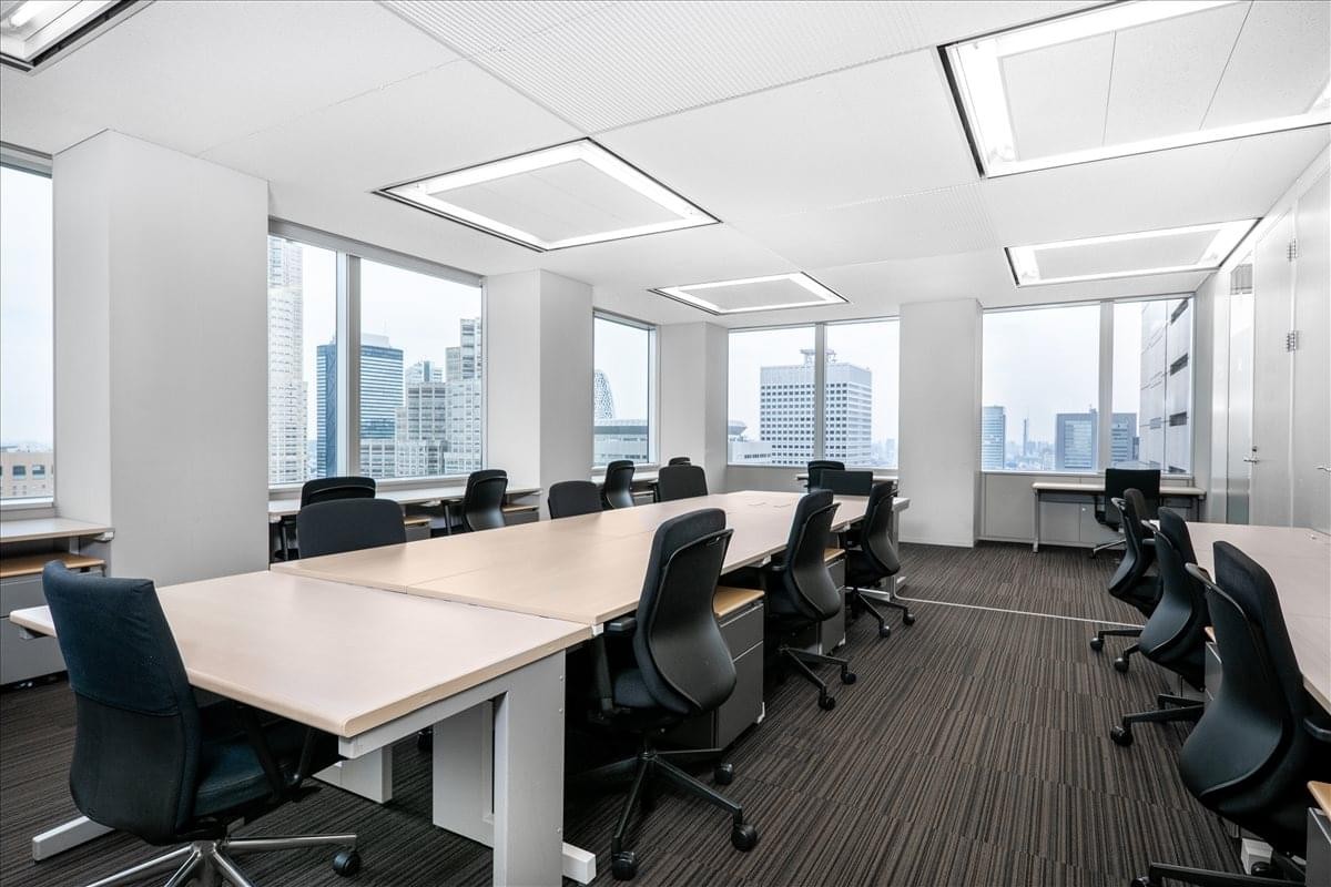 Bright open-plan coworking space with long shared desks and panoramic city views.