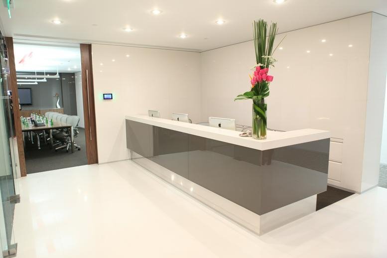 Modern minimalist reception desk with glossy gray panels and a tall floral arrangement.