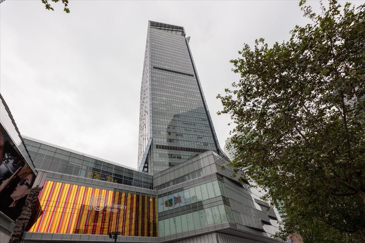 A dramatic low-angle view of the glass-facade Yanlord Landmark Office Tower skyscraper against a cloudy sky.