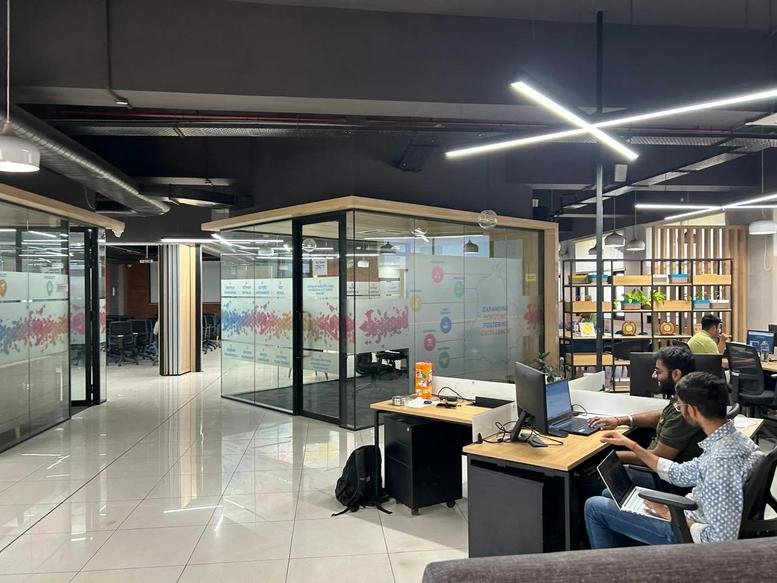 Modern open-plan workspace at Plot 129 / 1 with glass-walled private booths and collaborative desk areas.