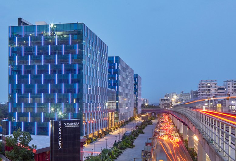 Exterior view of the blue glass facade at Redbrick Offices, Sumadhura Capitol Towers with city traffic lights.