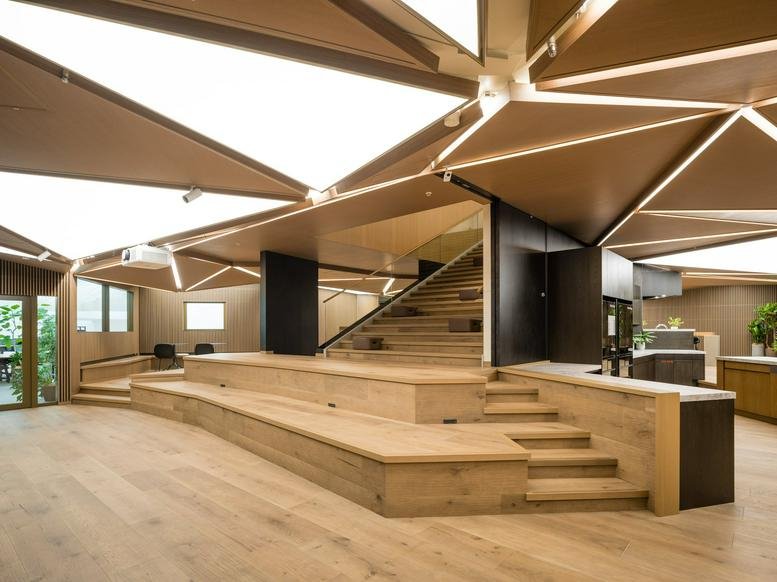 Large wooden amphitheater seating area at Toranomon Hills Business Tower with geometric light panels.