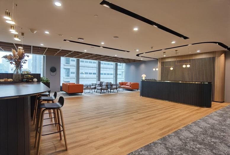 Modern reception lobby with warm wood floors, a long dark front desk, and orange lounge seating.