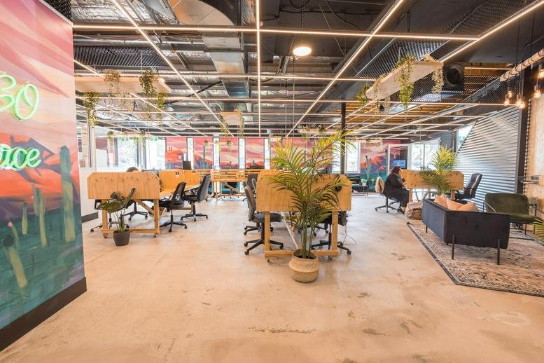 Spacious coworking area at 10-14 Wormald Street, Symonston ACT, Canberra with desks, plants, and sunset murals.