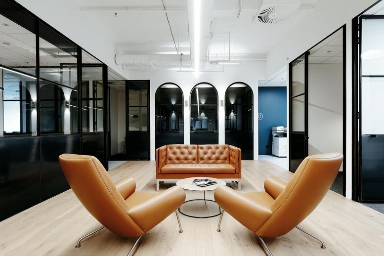 Spacious communal lounge at Genworth Building, 101 Miller Street with tan leather chairs and arched windows.