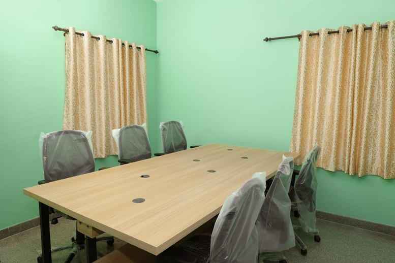 Meeting room at 102, Sathy Road, featuring a large wooden table and grey ergonomic chairs against green walls.