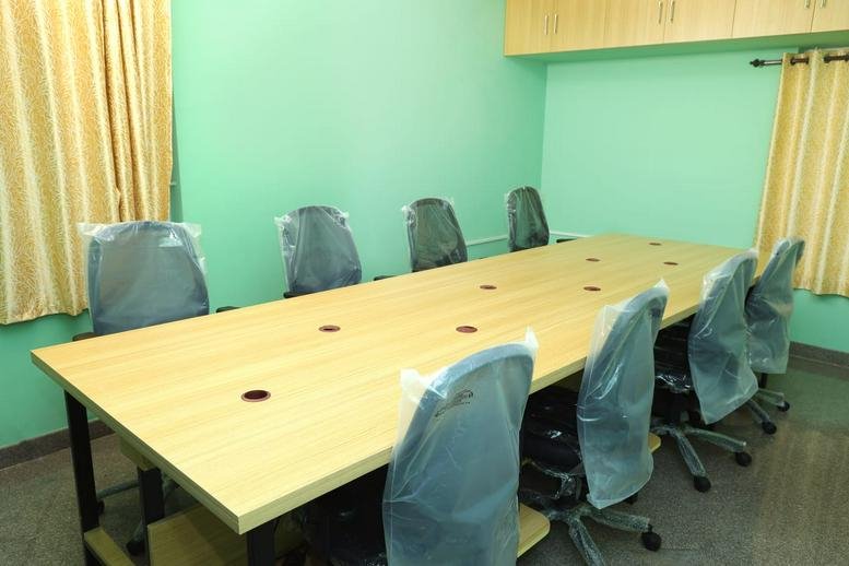 Spacious conference room at 102, Sathy Road featuring a long light wood table and ergonomic mesh seating.