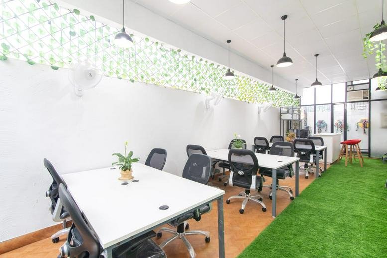 Bright coworking space with multiple desks and green carpet.