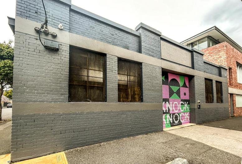 Exterior street view of a grey brick industrial-style building with colourful geometric mural art.