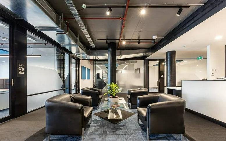 Modern lobby at Level 1, 115 Bridge Road with industrial ceilings, black leather armchairs, and glass partitions.