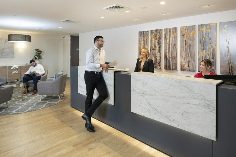 Reception area with a marble desk and three people interacting.