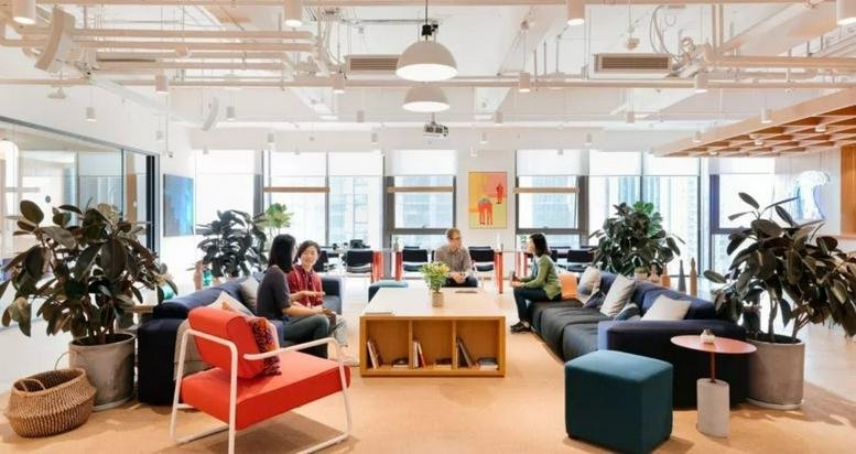 Spacious sunlit lounge area with comfortable sofas, potted plants, and an open ceiling design.