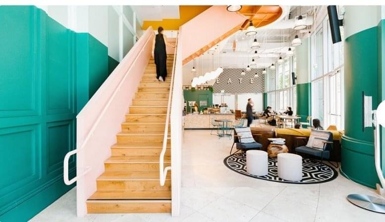 Spacious reception area at 11th Avenue with a pink staircase, teal walls, and modern lounge seating.