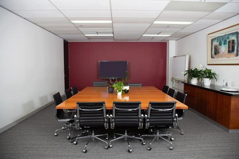 Large conference room with a red feature wall, square wooden table, and black ergonomic chairs.