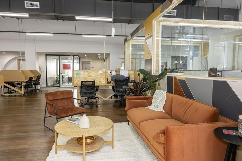 Spacious coworking lounge with velvet seating, a white rug, and view of hot desks.