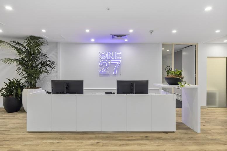 Sleek white reception desk with violet glowing logo and potted palms.