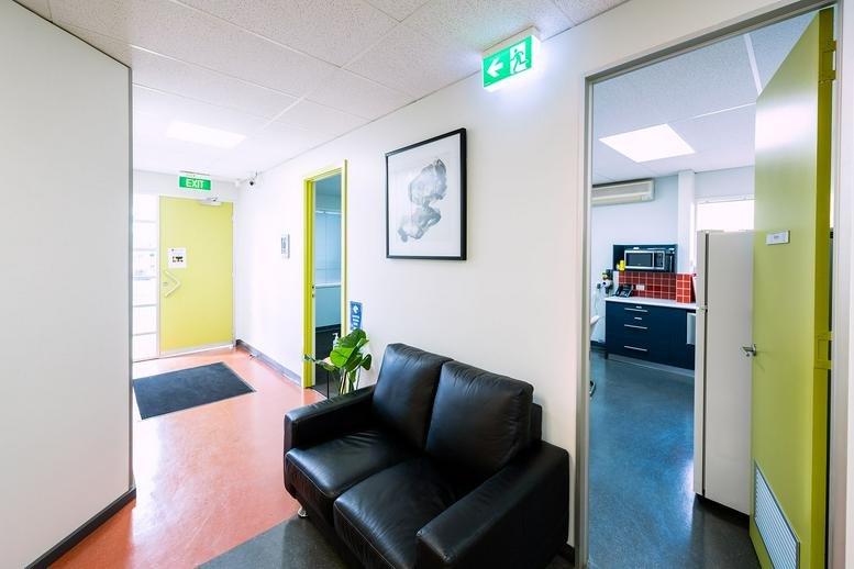 Reception area with black leather sofa and view into a communal kitchen area.