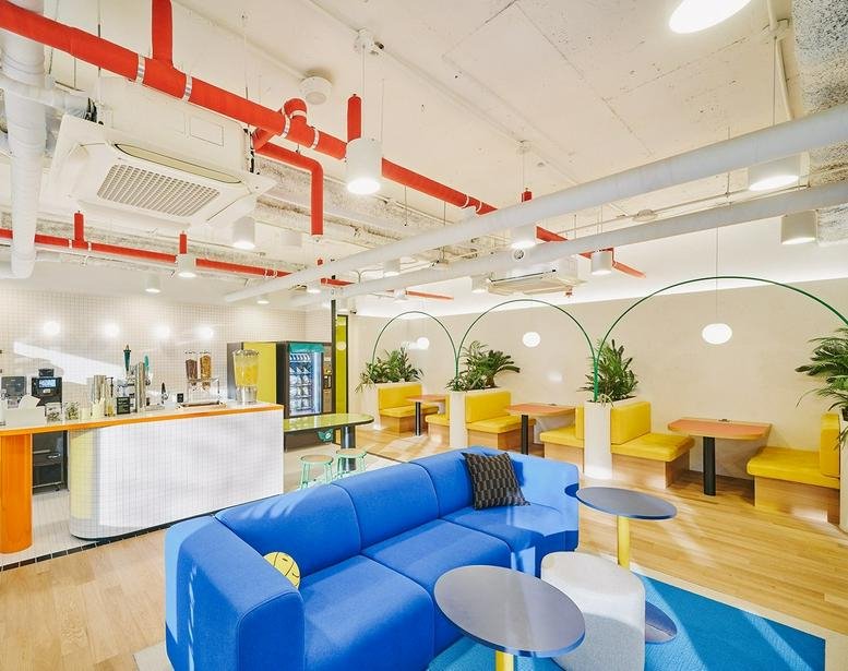 Spacious communal lounge at 151, Teheran-ro, Yeoksam 3 with a blue modular sofa, yellow booths, and red exposed piping.