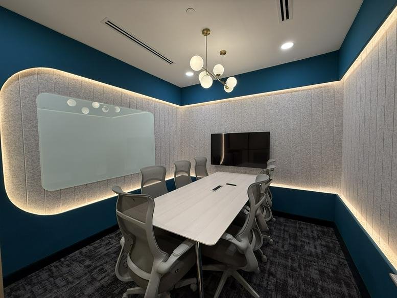 Meeting room with a white table, grey mesh chairs, and dark blue accent walls.
