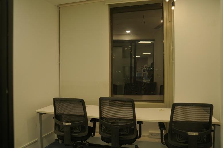 Small meeting room with a white desk and a large window looking into the office.