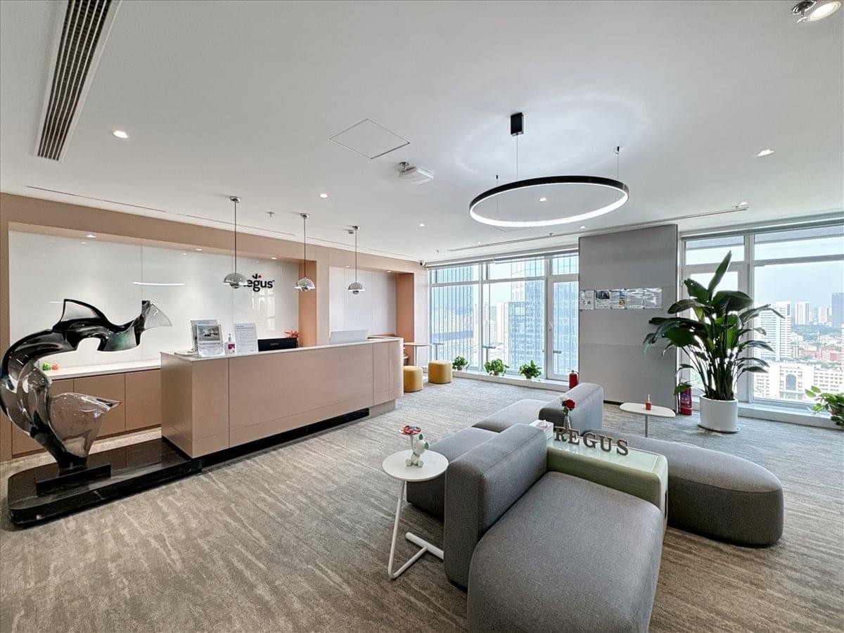 Bright lobby with a wooden front desk, grey lounge seating, and floor-to-ceiling windows.
