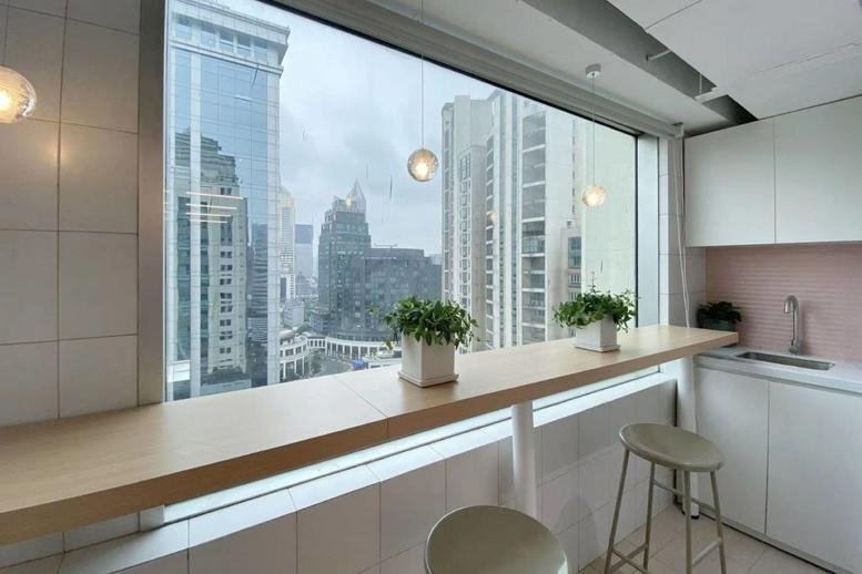 Bright breakout space at Jing An New Century Building with a window-facing wood bar and city views.