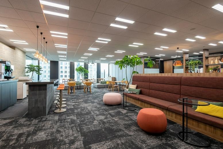 Spacious communal lounge with a coffee bar, long cushioned bench, and colorful ottoman seating.