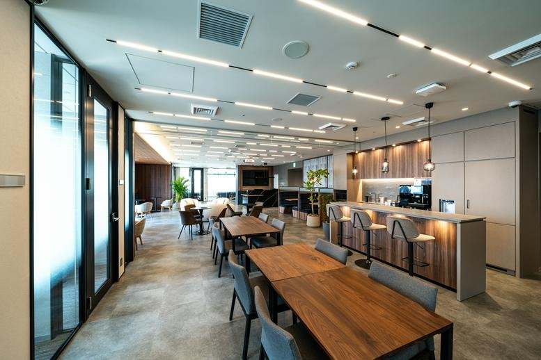 Modern communal breakout area with cafe seating, long wooden tables, and a breakfast bar.