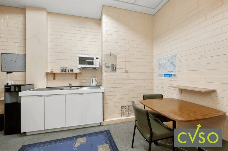 Staff kitchen and breakout area with white cabinetry and a wooden dining table.