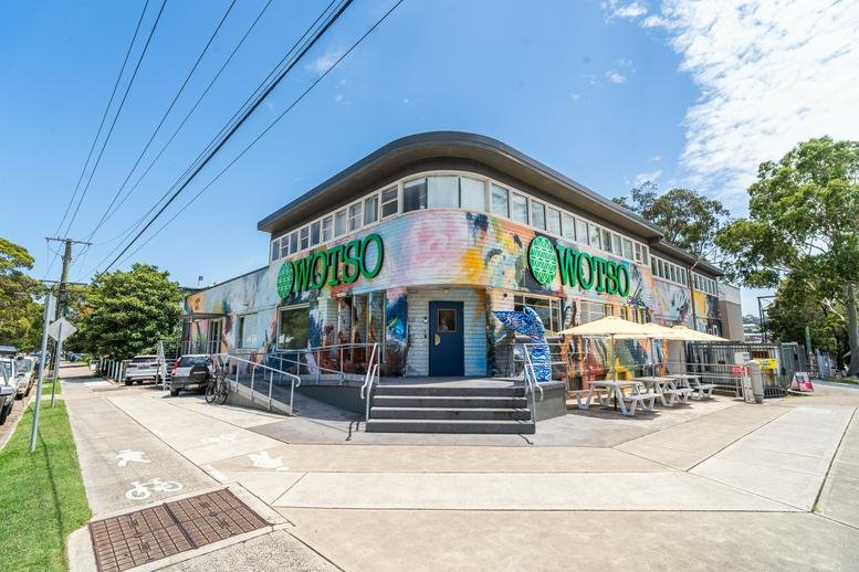 Street view of the rounded corner building with WOTSO signage and outdoor seating.