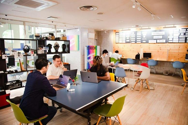 Spacious communal coworking area at 2-chōme-1-1 Minamihonmachi, Osaka with people working at a large blue table.