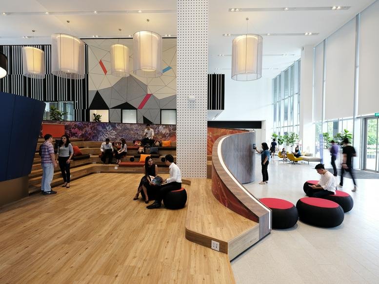 Spacious communal lounge at 2, Science Park Drive with stepped wooden seating and modern pendant lights.