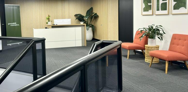 Reception area at 213 Greenhill Road featuring a white front desk, orange armchairs, and lush green plants.