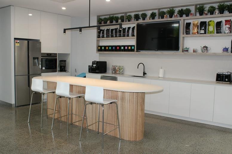 Modern communal kitchen and break area with a wooden island and white stools at 214 Bay Street, Brighton.