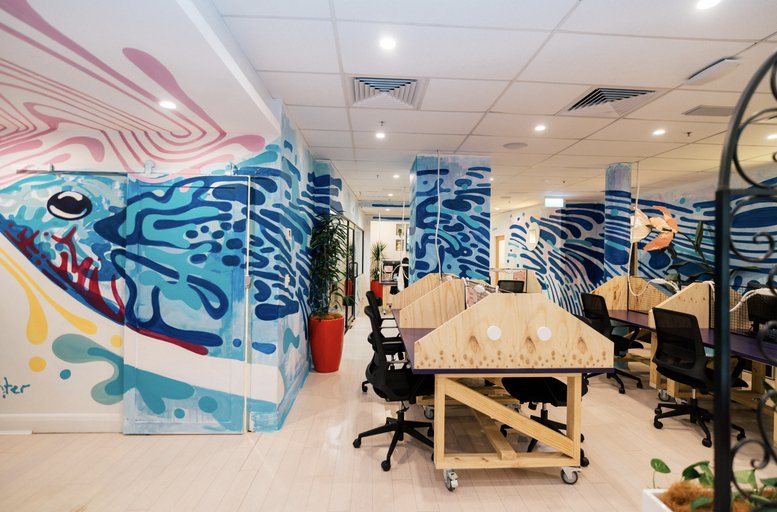 Spacious coworking area with wooden desks, ergonomic chairs, and vibrant wall murals at Level 1, 222 Pitt Street.