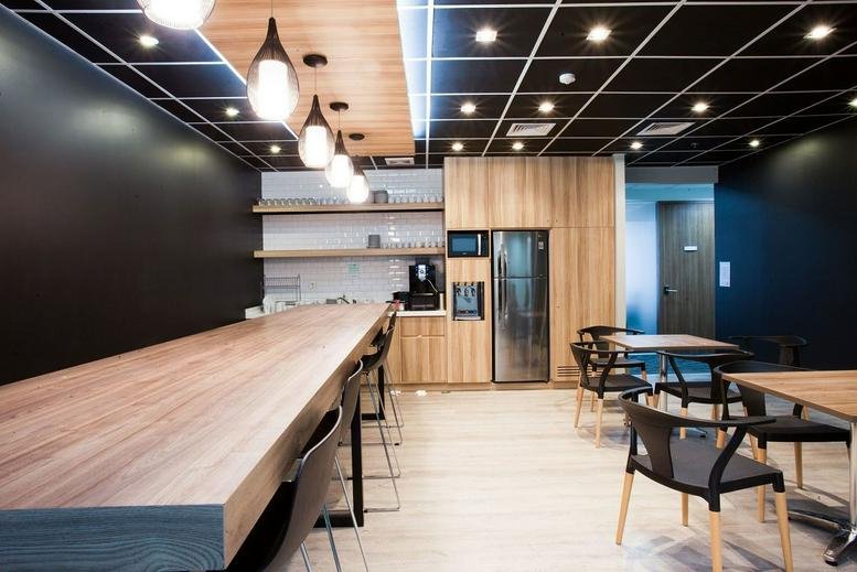 Communal break area with a long wooden high-top table and modern pendant lighting.