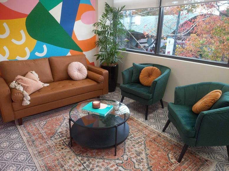 Colorful lounge at 244 Macquarie Street, Level 1, featuring a mural, tan sofa, and green velvet armchairs.