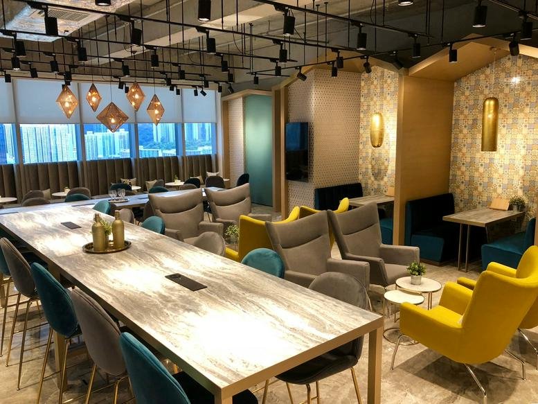 Spacious communal lounge featuring a long wooden table, teal and yellow armchairs, and city views.