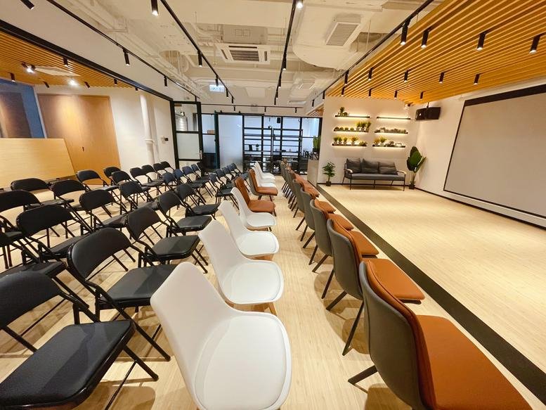 Spacious event hall at Delta House featuring rows of black and white seating and a large projection screen.