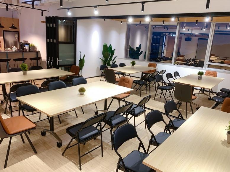 Vibrant coworking area with multiple light wood tables, colourful chairs, and natural greenery.