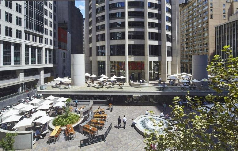 Wide view of a bustling urban plaza with outdoor seating and umbrellas between city buildings.