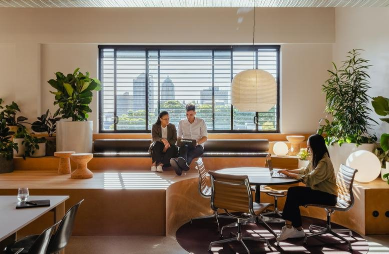 Spacious communal lounge with tiered wooden seating, round tables, and large orb pendant lighting.