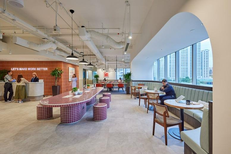 Spacious communal lounge and coworking area at Central Plaza with a long pink tiled table and arched windows.