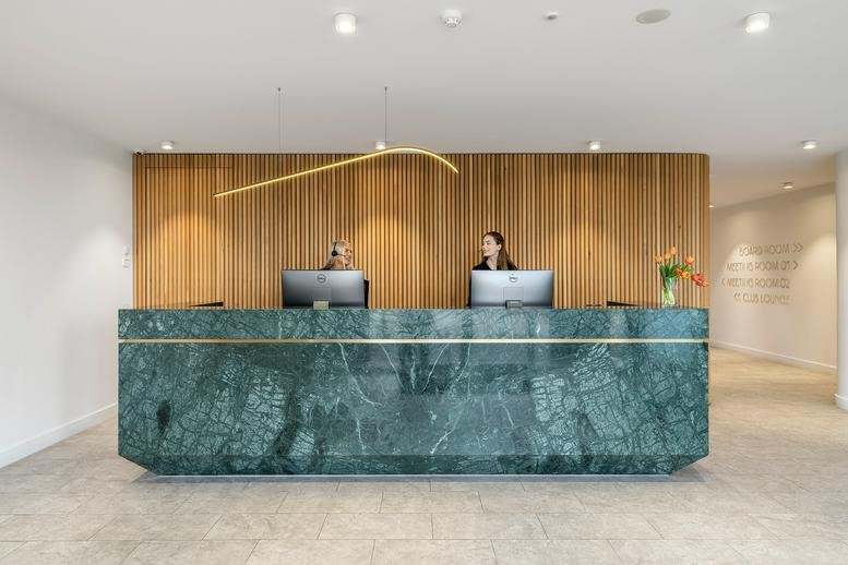 Polished reception area at 2A Westall Road featuring a large green marble desk and wood paneling.