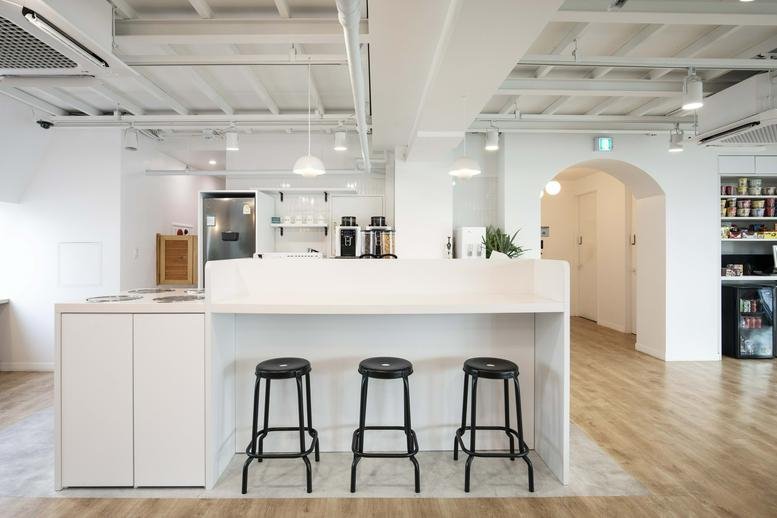 Modern communal kitchen and cafe area with white counters and black bar stools at 303 Gonghang-daero.